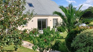 A house with a sloped roof, a small garden with various plants, and a paved pathway leading to the entrance.