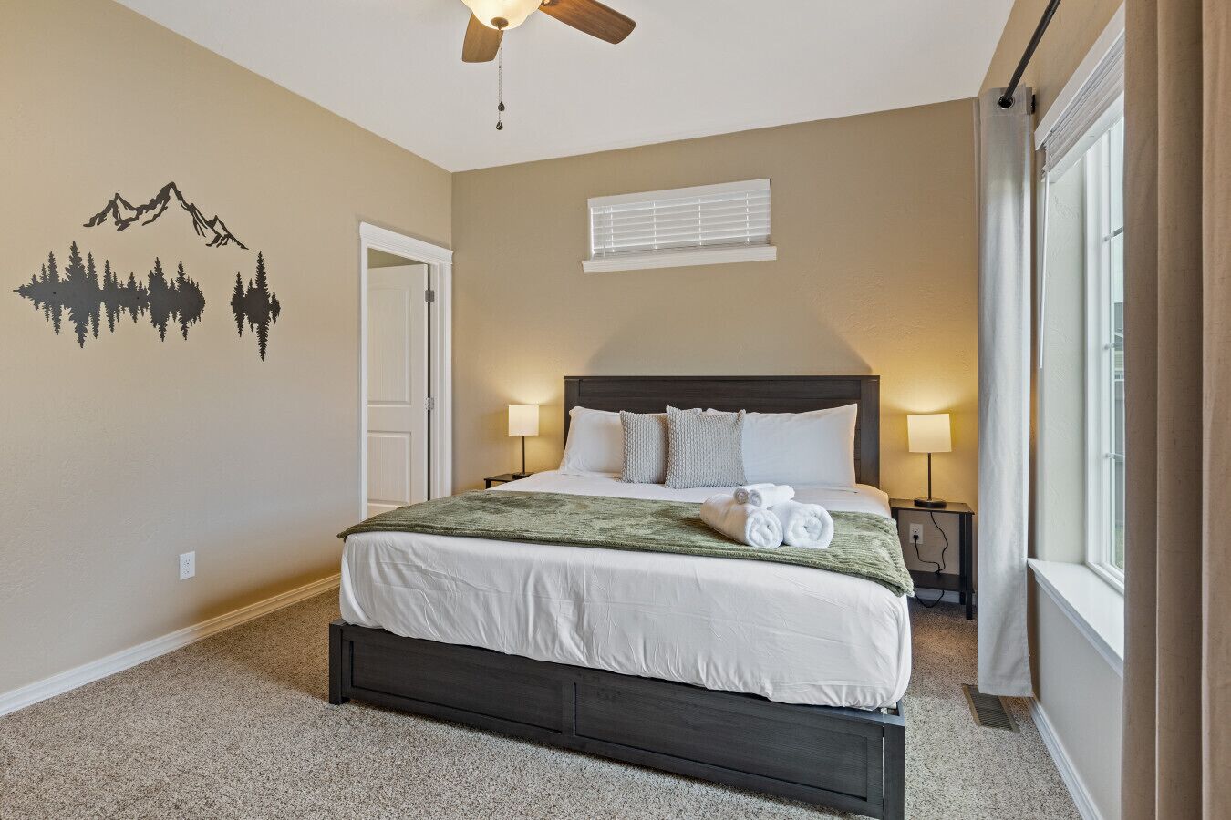 A bedroom with a bed, two bedside lamps, a window, and a ceiling fan.