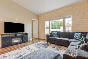 A living room with a fireplace, a gray sofa with patterned cushions, and a large flat-screen TV on a wooden entertainment unit. - Central Kalispell Family Retreat w/ Big Backyard (Kalispell)