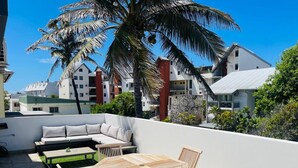 A rooftop patio with a wooden table and chairs, a sofa, and a small coffee table. - ALIZEA apartment, spacious with large terrace (Saint-Pierre)