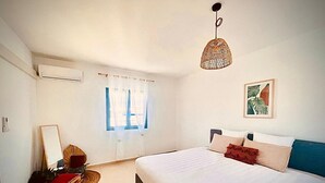 A bedroom with a large bed, a hanging light fixture, a window with sheer curtains, and a framed picture on the wall. - ALIZEA apartment, spacious with large terrace (Saint-Pierre)
