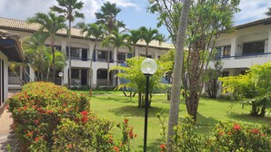 A courtyard with a lawn, palm trees, and red flowering bushes.