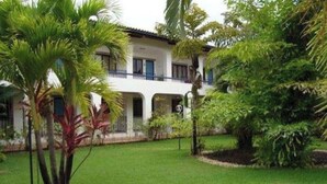 A two-story building with a balcony, surrounded by lush greenery and a well-maintained lawn.