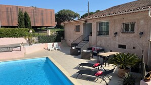 A swimming pool with lounge chairs, a covered patio area, and a building with a tiled roof. - T2 apartment in condominium (Villa) with pool access (Fréjus)