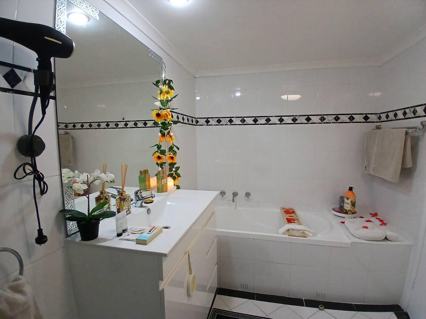 A bathroom with a white sink, mirror, and bathtub. There are toiletries on the sink and a towel rack on the wall.