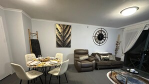 A dining area with a round table set for six, a brown leather sofa, and a decorative clock on the wall.