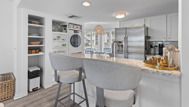 Een moderne keuken met witte kasten, een roestvrijstalen koelkast, een ingebouwde oven en een groot eiland met barkrukken.