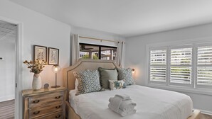 Een keurig opgemaakt slaapkamer met een bed, nachtkastje en een raam met zonwering.