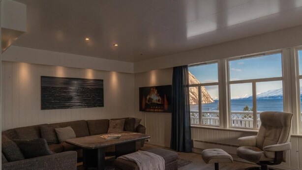A modern living room with a large window, a sofa set, a coffee table, and a chair. - Lyngen Aurora House (Lyngseidet)