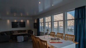 A modern living room with a dining area, large windows, and a view of mountains. - Lyngen Aurora House (Lyngseidet)