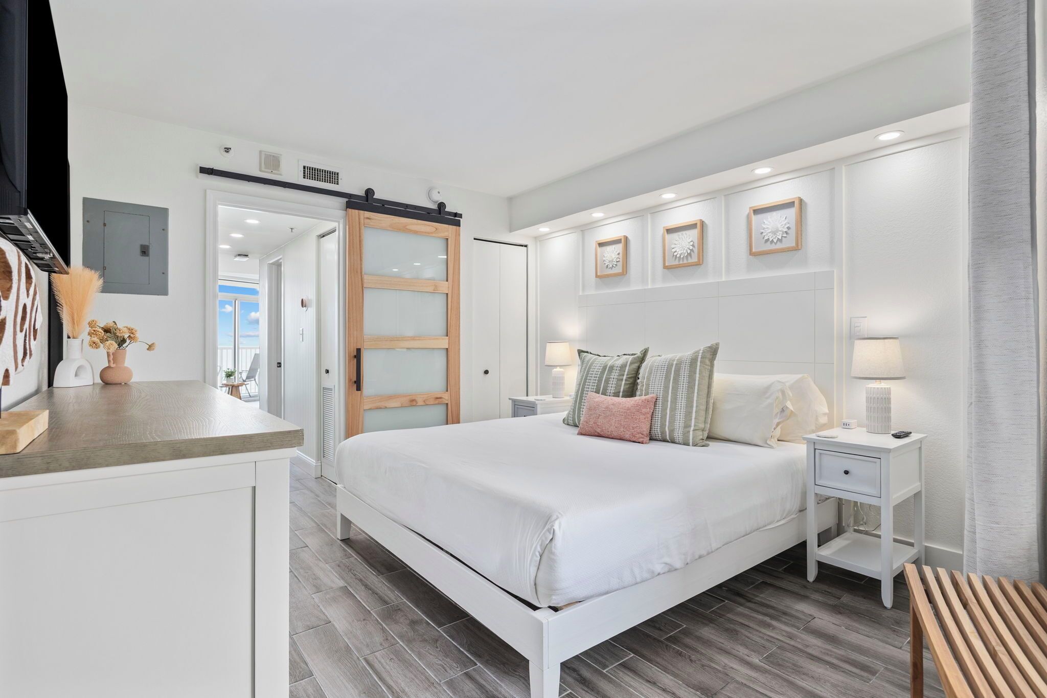 Un dormitorio con cama, mesitas de noche, un banco de madera y una puerta corredera que da a otra habitación.