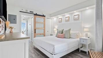 Un dormitorio con cama, mesitas de noche, un banco de madera y una puerta corredera que da a otra habitación.