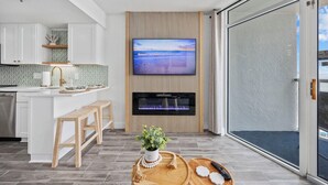 A modern kitchen with a built-in TV, wooden bar stools, and a potted plant on a wooden tray.