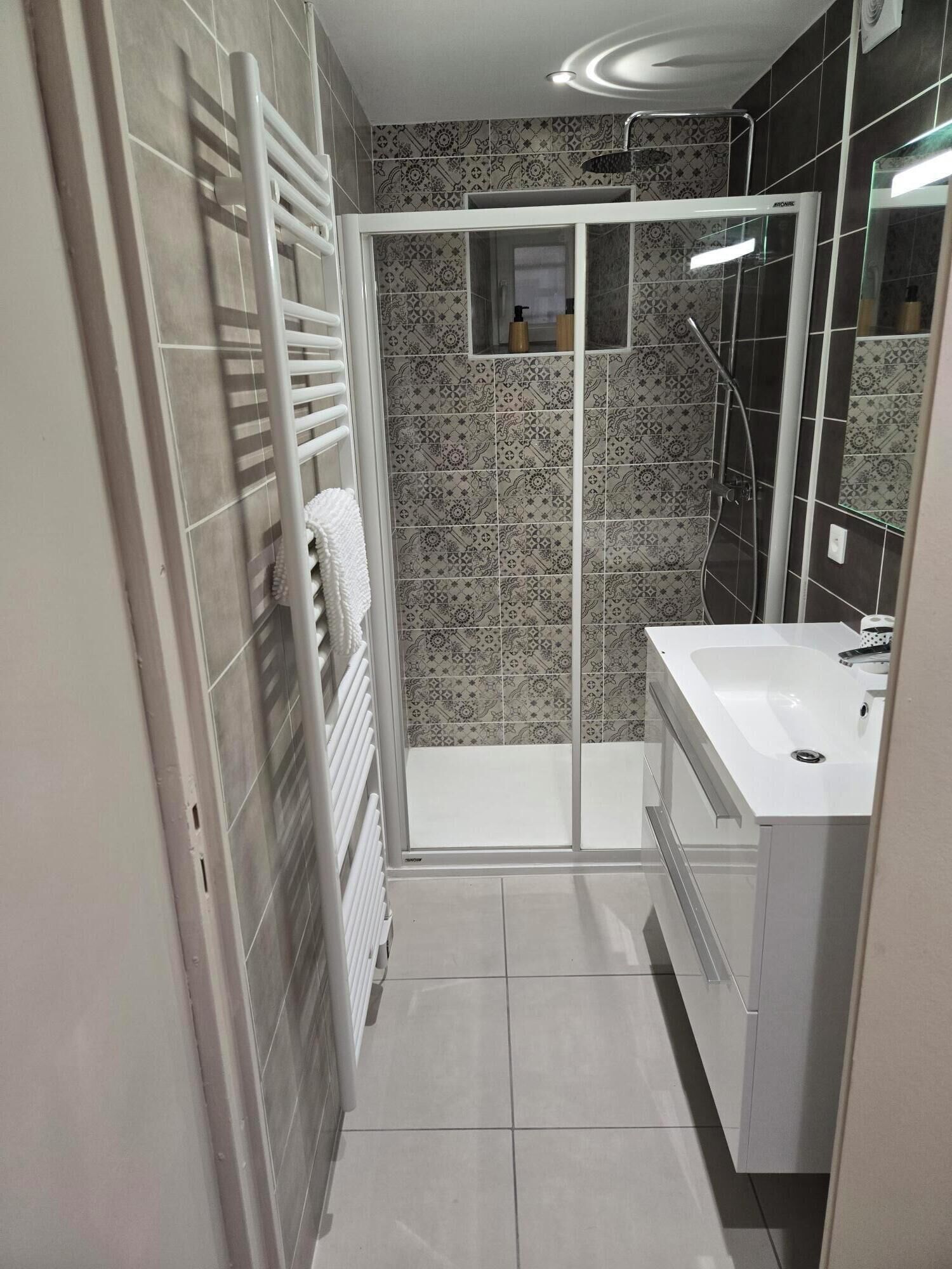 Une salle de bain moderne avec une douche, un lavabo blanc et un porte-serviettes.