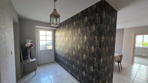 A hallway with a patterned wall, a door, a small table with a vase, and a chair.