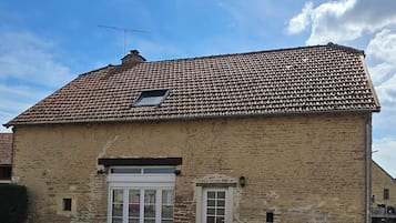 A two-story stone building with a tiled roof, a small window, and a door.