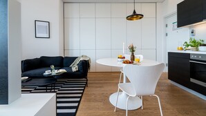 Um espaço de estar moderno com um sofá preto, mesa de jantar branca e cozinha com forno embutido.