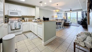 A modern kitchen with white cabinets, a central island, and a dining area with a view. - Disney Coastal Condo (Orlando)