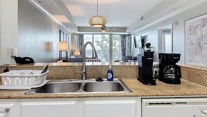 A modern kitchen with a granite countertop, double sink, and a coffee maker. - Disney Coastal Condo (Orlando)