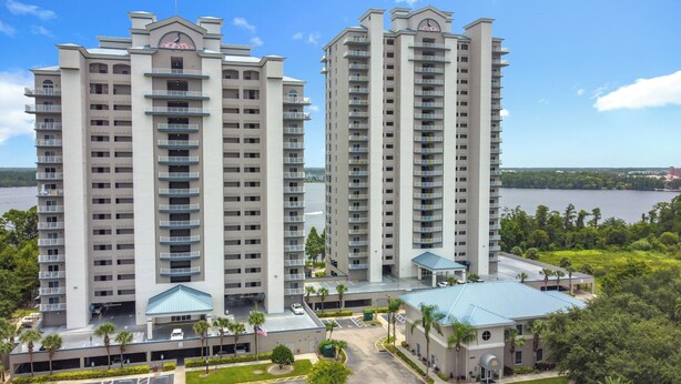 Two high-rise residential buildings with balconies, a parking area, and a view of a body of water. - Disney Coastal Condo (Orlando)
