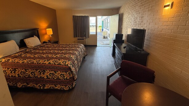 A hotel room with a large bed, a TV, a desk, and a chair. - ECONOMY INN (Belleville)