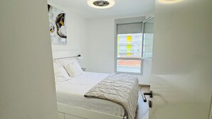 Ein Schlafzimmer mit Bett, einem Fenster mit Jalousien, einem Deckenventilator und Blick auf das äußere Gebäude.