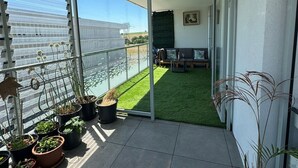 Ein Balkon mit Blumentöpfen, einer kleinen Sitzecke und Blick auf die Stadtlandschaft.