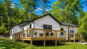 A white cabin with a wooden deck, surrounded by trees. - Creekside Retreat • Fire Pit | Patio | Arcade (Old Fort)