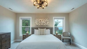 A bedroom with a large bed, two nightstands, a dresser, and a chandelier.