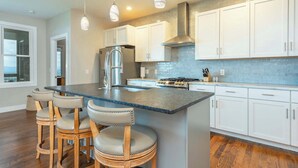A modern kitchen with white cabinets, a central island with bar stools, stainless steel appliances, and pendant lighting.