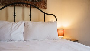 Un letto con lenzuola bianche, una testiera in metallo nero e un comodino con una lampada.