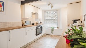 Una cucina moderna con mobili bianchi, un piano di lavoro in legno, forno integrato, microonde e una finestra con persiane.