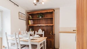 Un'area pranzo con tavolo in legno apparecchiato per quattro persone, sedie bianche, una libreria in legno e un armadietto bianco.
