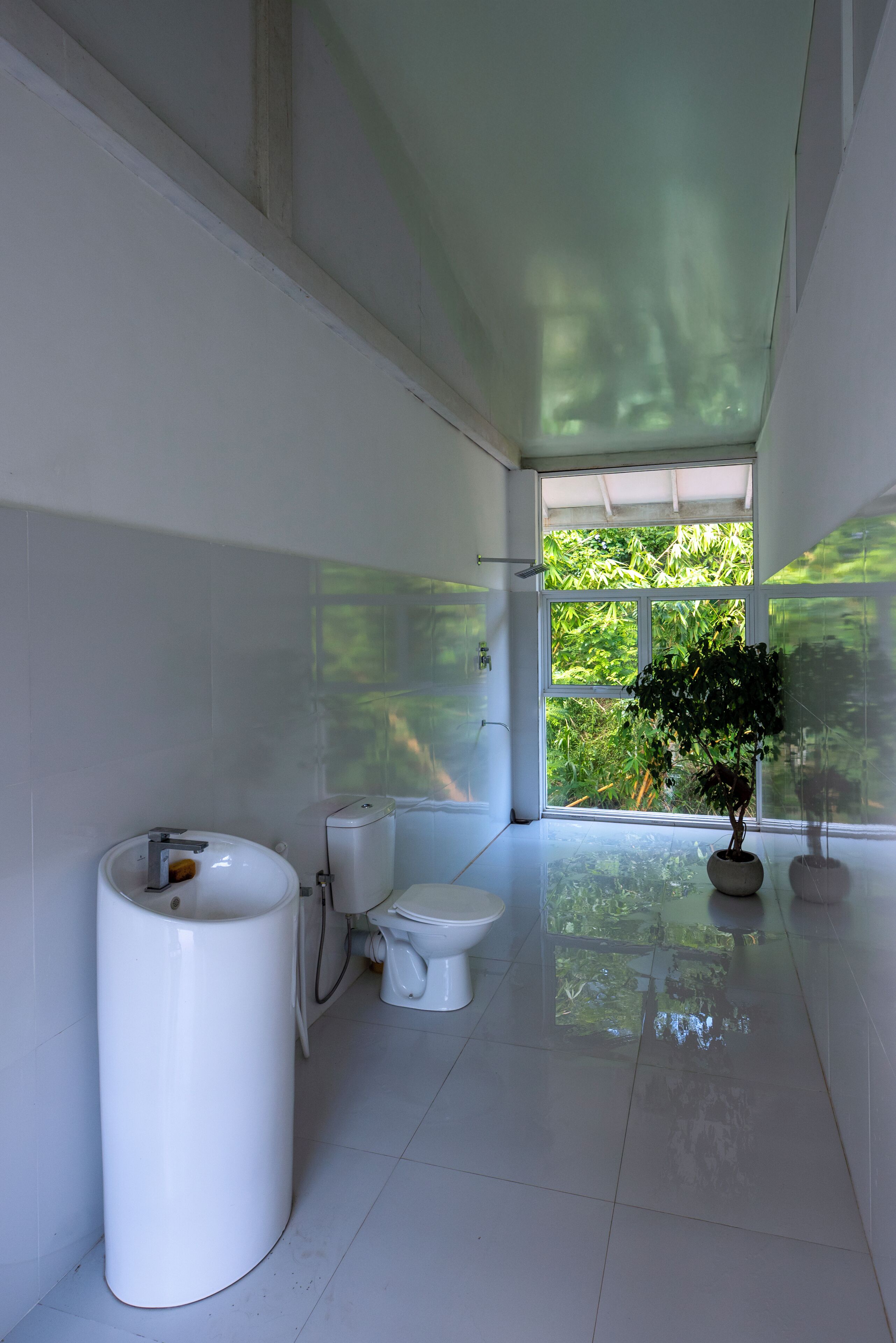 Un baño moderno con inodoro, bidé y lavamanos. Una ventana grande ofrece vistas a la vegetación exterior.