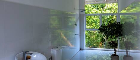 Un baño moderno con inodoro, bidé y lavamanos. Una ventana grande ofrece vistas a la vegetación exterior.