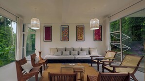 A modern living room with a sofa, chairs, and a coffee table. There are large windows with a view of greenery outside. - Colonial-style bungalow with private pool, mountain views  and tranquil vibes. (Kandy)