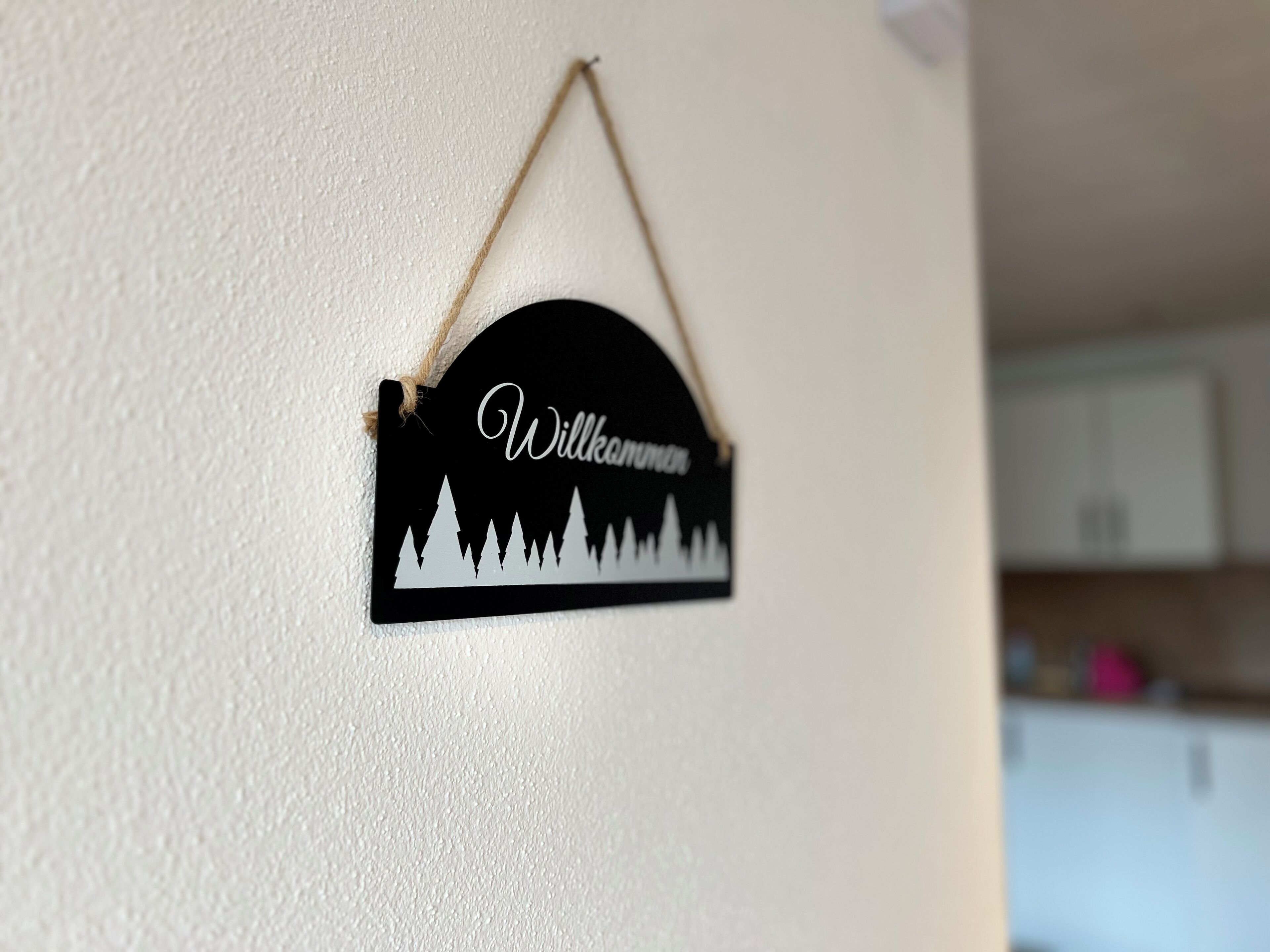 Een zwart welkombord met witte tekst en een silhouet van bomen op een witte muur.