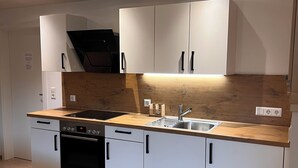 A modern kitchen with white cabinets, a wooden countertop, a Bosch dishwasher, and a built-in oven. - Vacation apartment Kink in Wiesweg, only 5 min to Rapunzel Welt, perfect for couples (Legau)