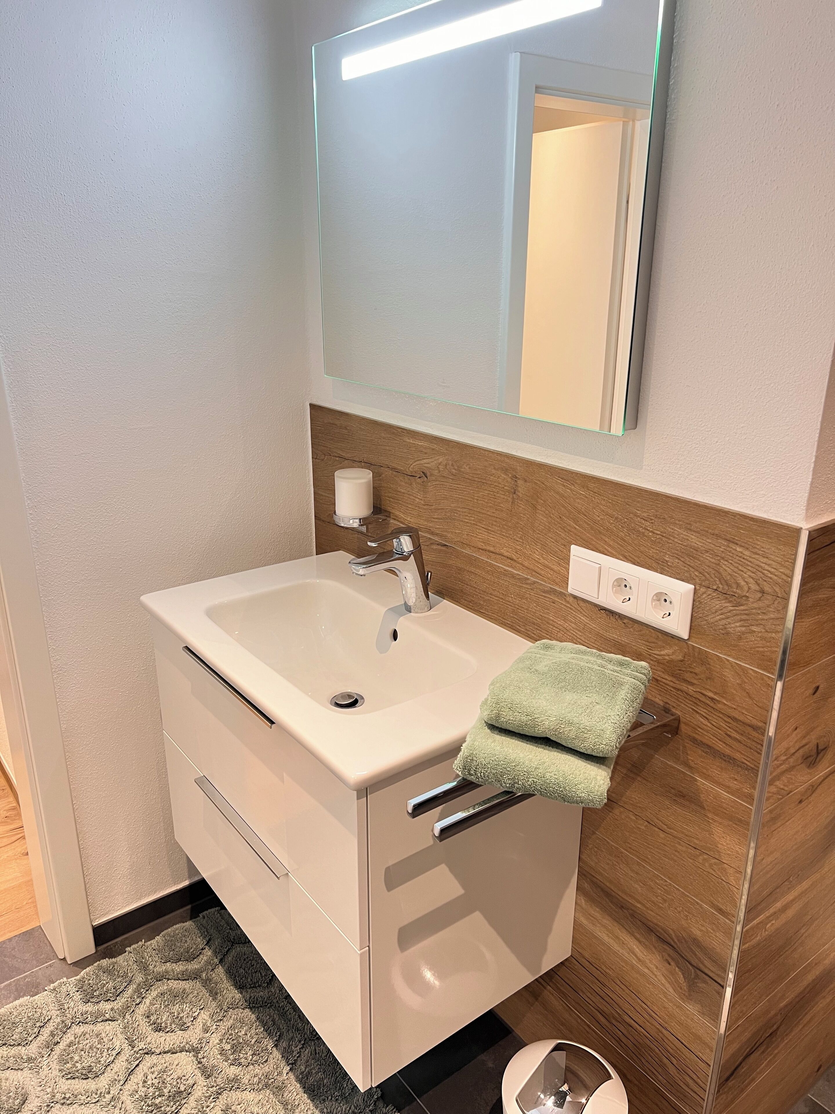 Een moderne badkamer met een witte wasbak, een spiegel en een houten opbergmeubel.