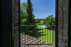 Un balcon avec un mur en pierre, une rambarde en métal et une vue sur une piscine et une pelouse verdoyante.