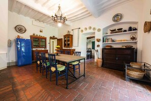 A rustic kitchen with a wooden table, chairs, a blue refrigerator, and a chandelier.