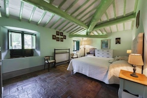 A bedroom with a large bed, a chair, a desk, a window, and a radiator.