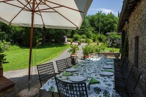 An outdoor dining area with a table set for four, surrounded by chairs, under a large umbrella.