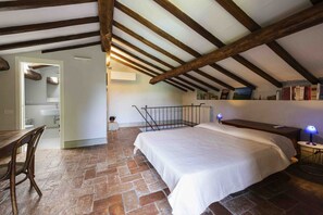 A bedroom with a stone floor, a bed, a desk with a chair, a bookshelf, and a staircase.