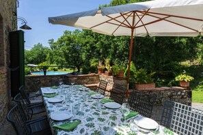 An outdoor dining area with a table set for four, surrounded by chairs, under a large umbrella.