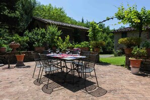 An outdoor patio with a table set for dining, surrounded by potted plants and a stone wall.