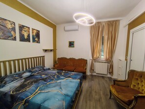 Een slaapkamer met een bed, een bank, een stoel, een radiator en een raam met gordijnen.