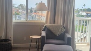 A living room with a sofa, a lamp, a small table, and a view of the outside. - Walkable Ocean-View Lantern District Home with AC & Garage (Dana Point)
