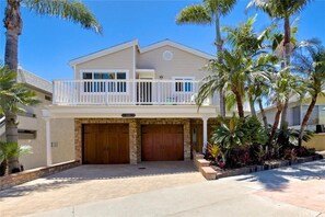 A two-story house with a balcony, a garage, and a well-maintained garden with palm trees.