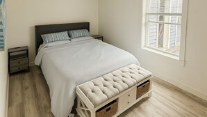 Ein Schlafzimmer mit einem Bett, Nachttischen, einem Deckenventilator, einem Fenster mit Jalousien und einem Holzboden.